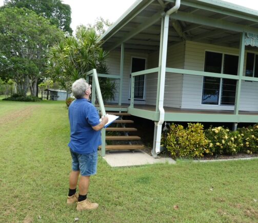 Certified building inspector conducting a visual pre-purchase inspection outside a property in Bowen, Queensland.